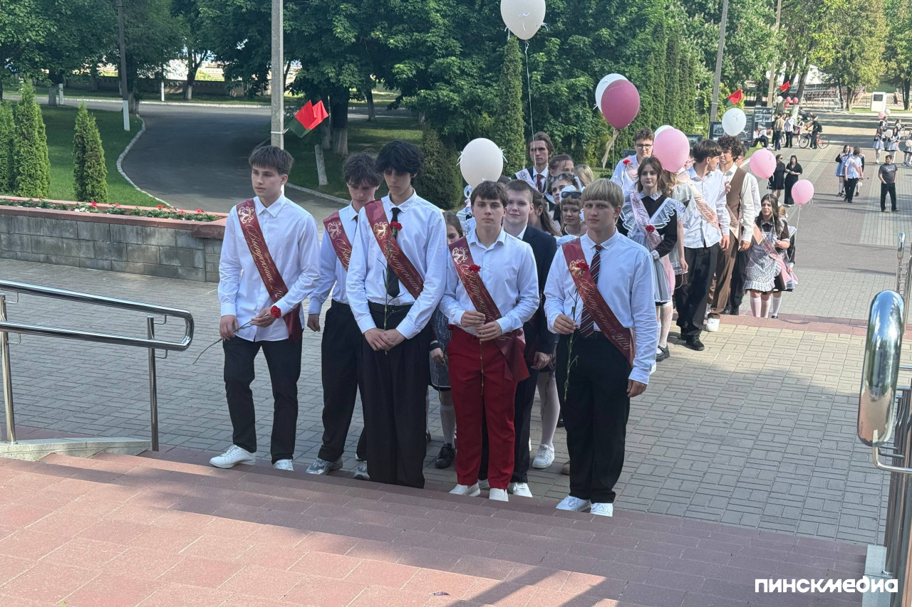 Пинские выпускники с праздничными лентами организованно идут по ступеням мемориала в городском парке культуры.