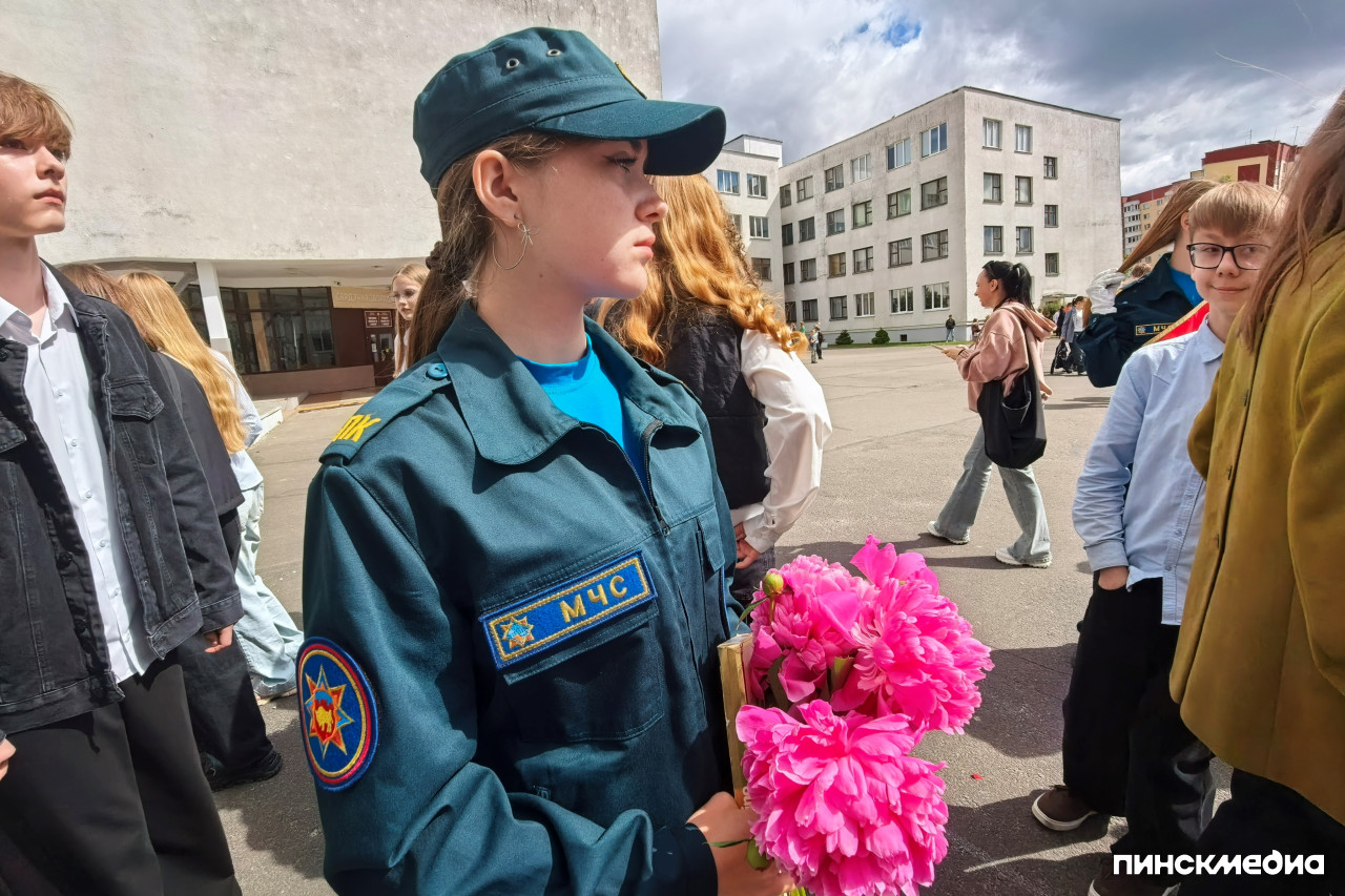 Девочка в форменной одежде МЧС с красной лентой держит букет розовых цветов.