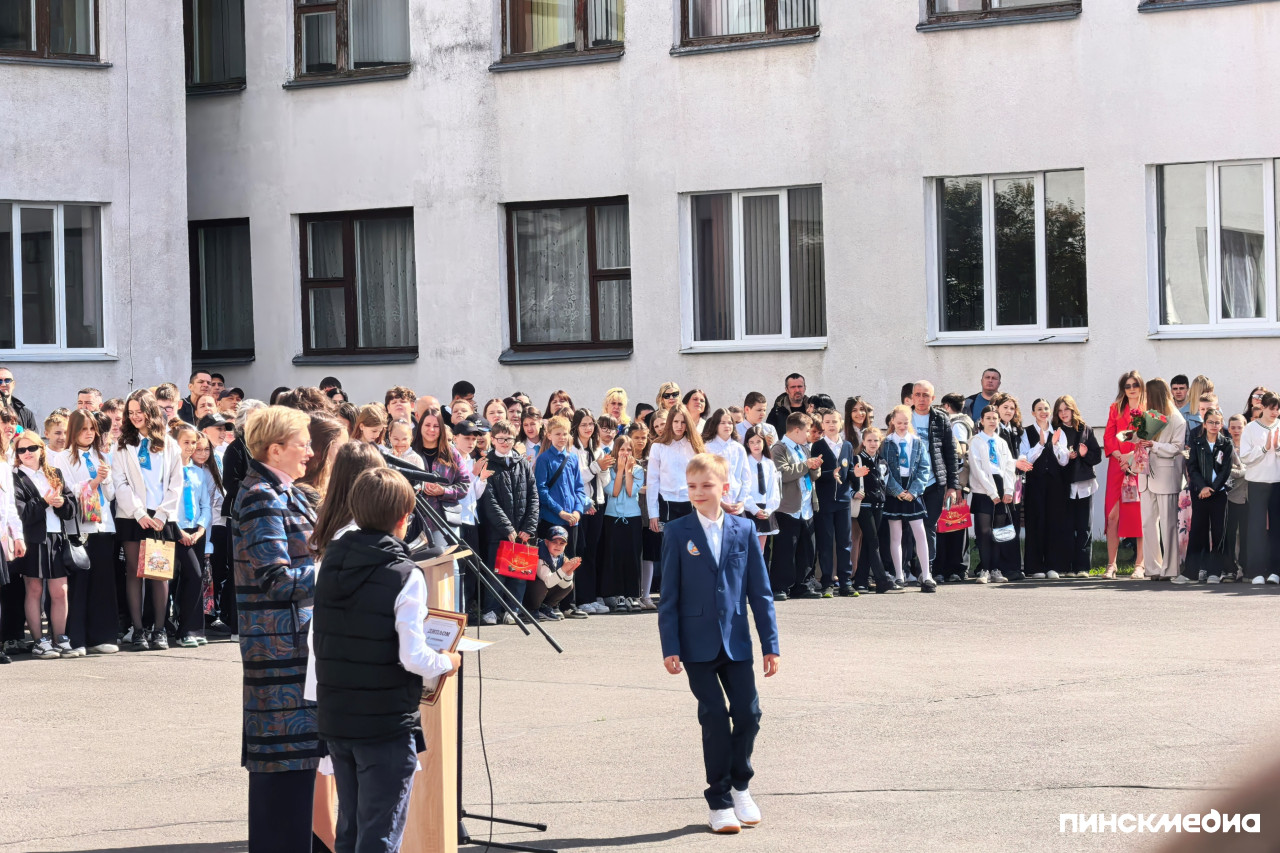 Широкий план школьного двора в солнечный день, ученики стоят в длинной шеренге.