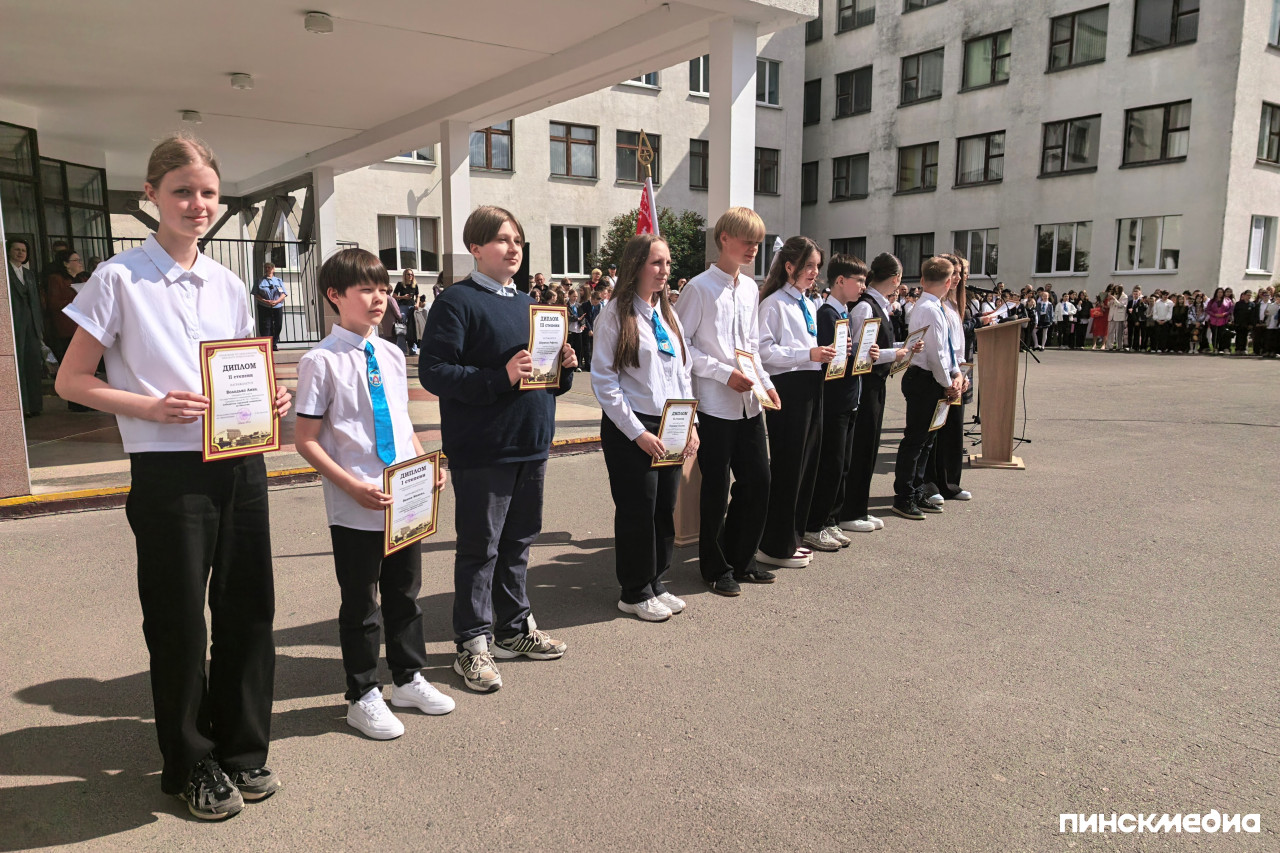 Ряд школьников в белых рубашках стоят на крыльце школы с дипломами в руках.
